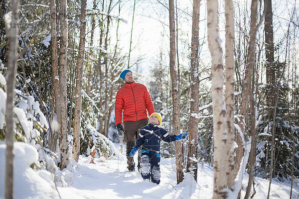 Mann und Sohn schauen auf  während sie durch den verschneiten Wald gehen