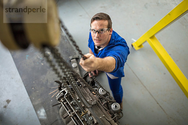 Draufsicht eines männlichen Automechanikers  der den Motor eines Windenautos in einer Reparaturwerkstatt repariert