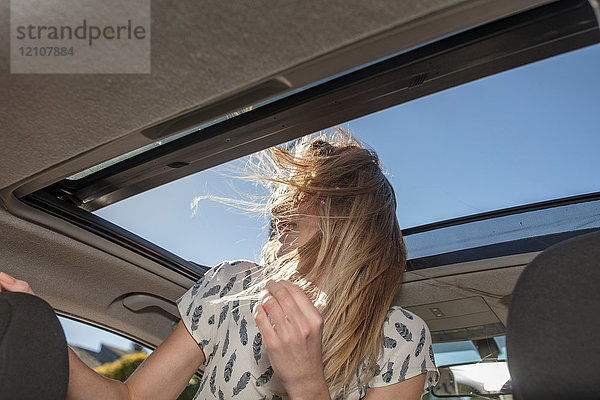 Junge Frau im Auto  die aus dem offenen Schiebedach schaut