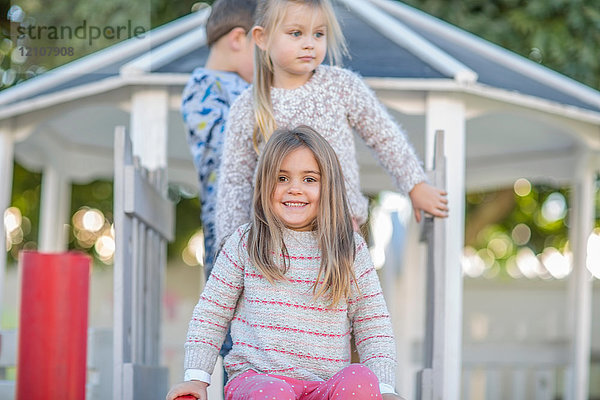 Mädchen und Junge in der Vorschule  Porträt oben auf der Spielplatzrutsche im Garten