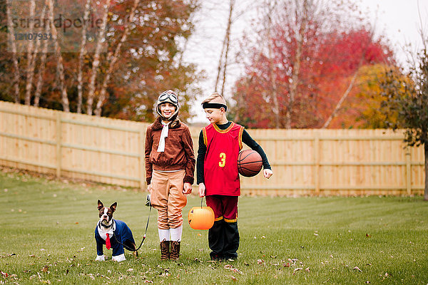 Porträt eines Jungen  einer Zwillingsschwester und eines Boston Terriers in Halloween-Kostümen im Garten