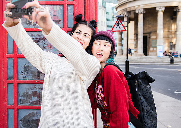 Zwei junge stilvolle Frauen beim Selfie an der roten Telefonzelle  London  UK