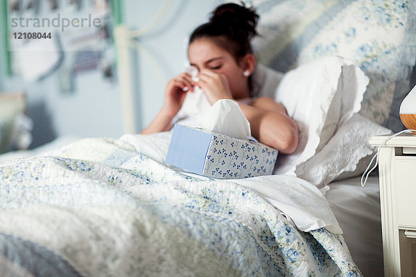 Mädchen im Bett schnäuzt Nase auf Taschentuch
