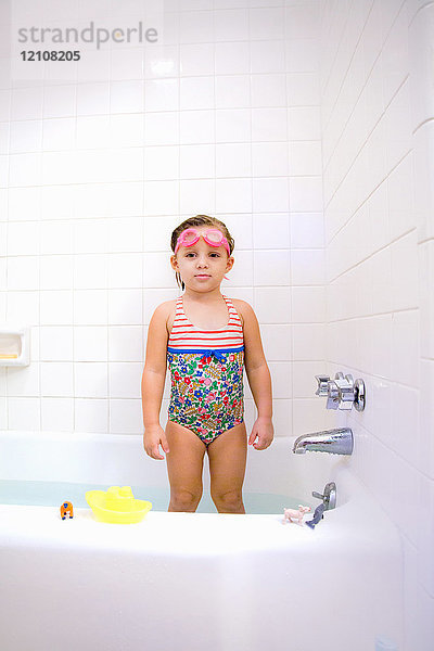 Porträt eines in der Badewanne stehenden Mädchens mit Schwimmbrille