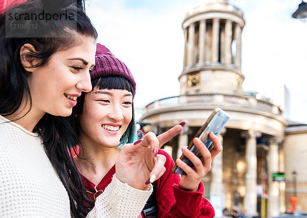 Zwei junge  stilvolle Frauen schauen sich ein Smartphone an  London  UK