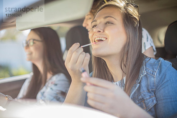 Junge Frau im Auto mit zwei Freunden  schaut in den Rückspiegel  trägt Lipgloss auf