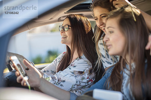 Junge Frau im Auto mit zwei Freunden  die ein Smartphone in der Hand halten