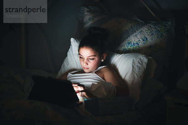 Mädchen im Bett  beleuchtet vom Licht des digitalen Tabletts