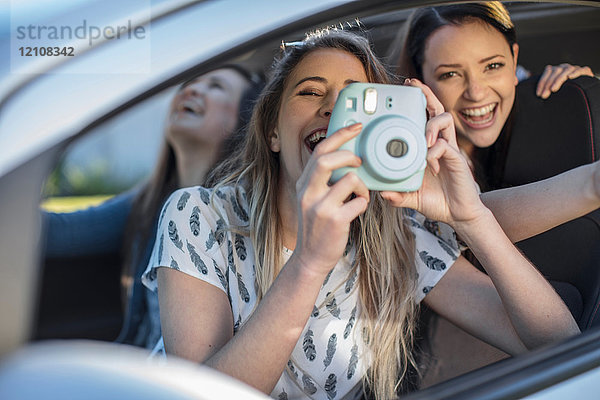 Junge Frau im Auto mit zwei Freunden  die aus dem Autofenster fotografiert