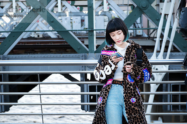 Stilvolle junge Frau betrachtet Smartphone auf der Millennium Footbridge  London  UK