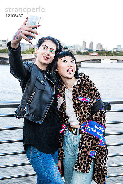 Zwei junge stilvolle Frauen beim Smartphone-Selfie auf der Millennium Footbridge  London  UK