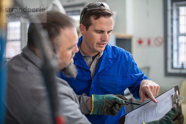 Männliche Automechaniker zeigen auf das Klemmbrett in der Reparaturwerkstatt