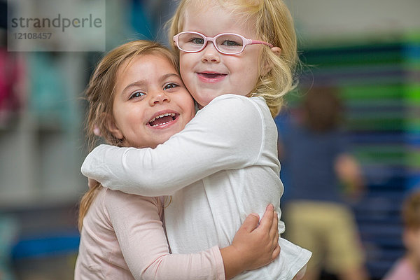 Porträt von zwei jungen Mädchen im Klassenzimmer  die sich umarmen