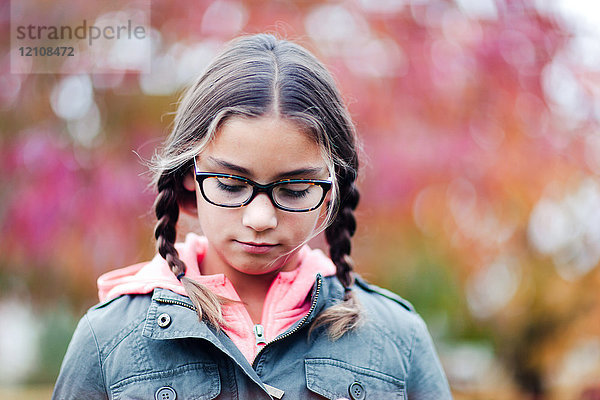 Porträt eines Mädchens mit Zöpfen und Brille mit Blick nach unten