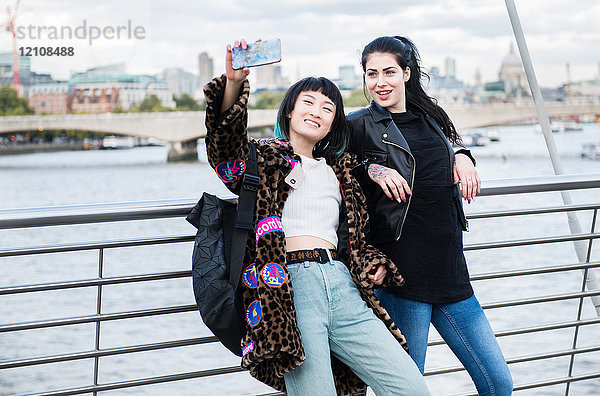 Zwei junge stilvolle Frauen beim Smartphone-Selfie auf der Millennium Footbridge  London  UK