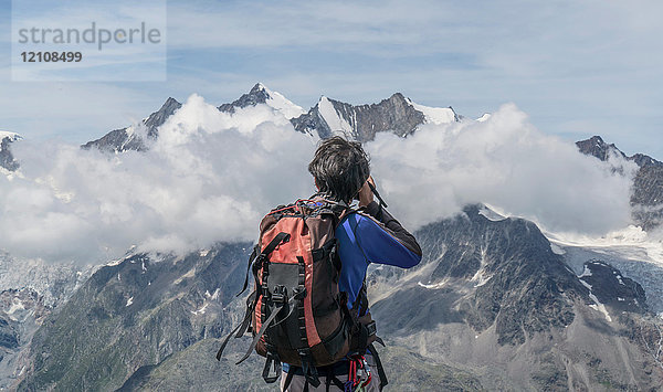 Rückansicht eines männlichen Bergsteigers beim Fotografieren von Mittelgebirgswolken am Jegihorn  Wallis  Schweiz