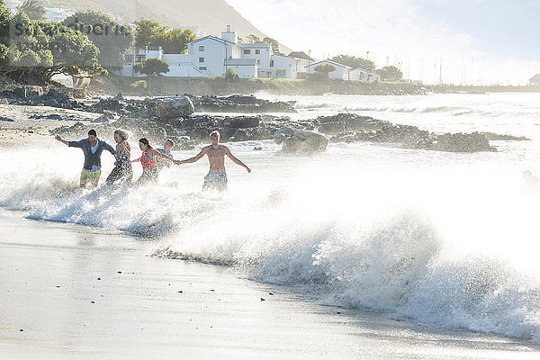 Junge erwachsene Freunde rennen und planschen bei Strandparty durch Wellen