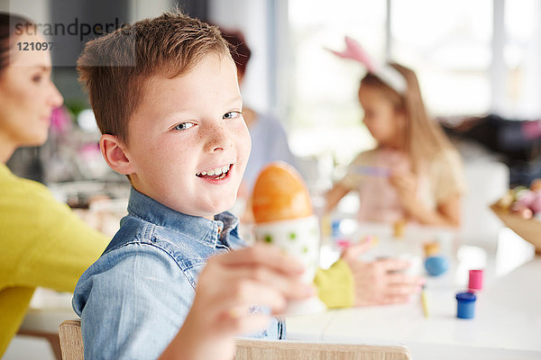 Porträt eines Jungen  der ein bemaltes hart gekochtes Osterei bei Tisch hält