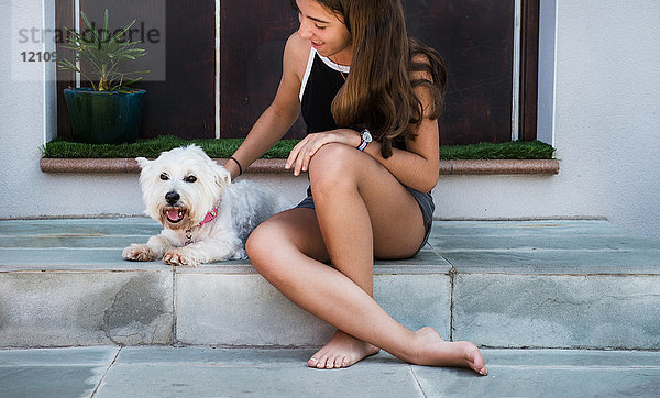 Teenager-Mädchen sitzt auf Terrassentreppe und streichelt Hund