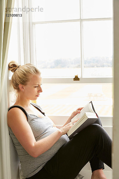 Schwangere Frau liest am Fenster