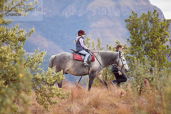 Mädchen reitet Pferd in ländlicher Umgebung  die Mutter geht an ihrer Seite