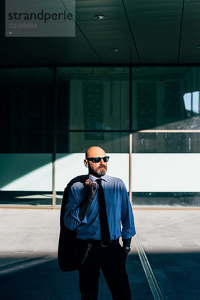 Porträt eines reifen Geschäftsmannes  der im Freien steht und eine Anzugsjacke über der Schulter trägt