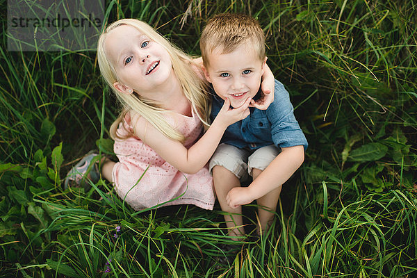 Junge und Mädchen sitzen zusammen im hohen Gras und schauen in die Kamera