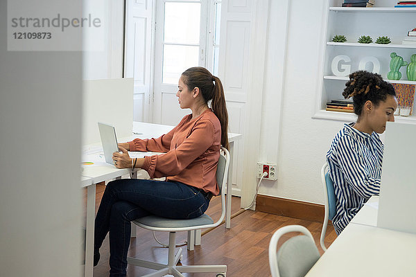 Zwei Geschäftsfrauen tippen am Büroschreibtisch auf Laptops