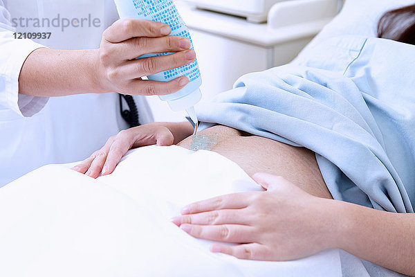 Schrägansicht des Sonographen  der das Gel auf den Bauch der schwangeren Patientin aufträgt