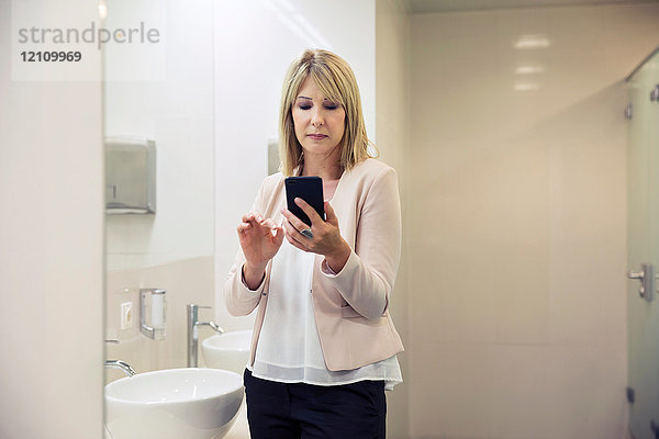 Frau benutzt Smartphone im Badezimmer