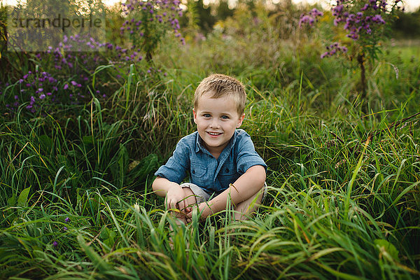 Porträt eines lächelnden Jungen  der im hohen Gras sitzt und in die Kamera schaut
