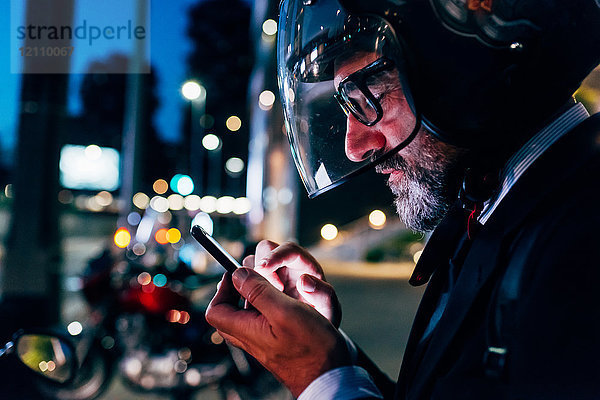 Reifer Geschäftsmann nachts im Freien  Motorradhelm tragend  Smartphone benutzen  Profil