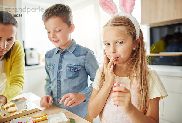 Mädchen leckt sich die Finger beim Zubereiten von Osterkeksen auf der Küchentheke