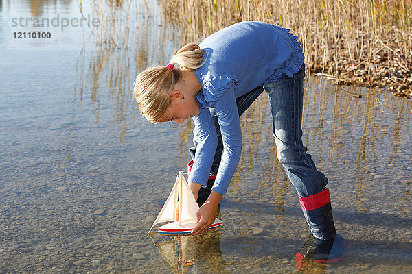 Junges Mädchen schwimmt Spielzeugboot auf dem Wasser