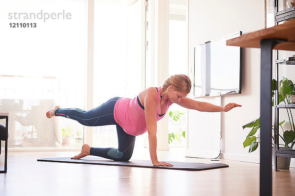 Schwangere junge Frau macht Yoga-Übungen im Wohnzimmer