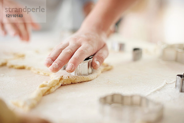 Hände eines Mädchens und einer Großmutter beim Ausstechen von Osterkeksen an der Küchentheke