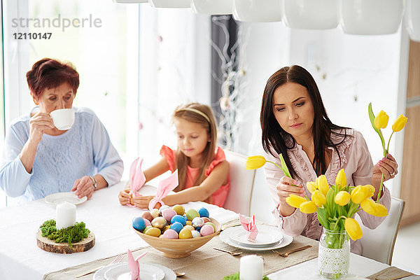 Frau mit Tochter und Mutter arrangiert gelbe Tulpen am Ostertisch