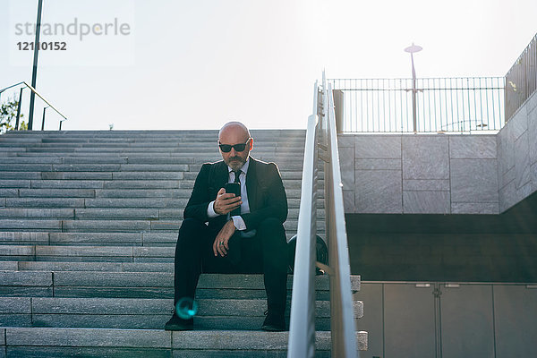 Reifer Geschäftsmann auf Stufen sitzend  mit Smartphone  niedriger Blickwinkel