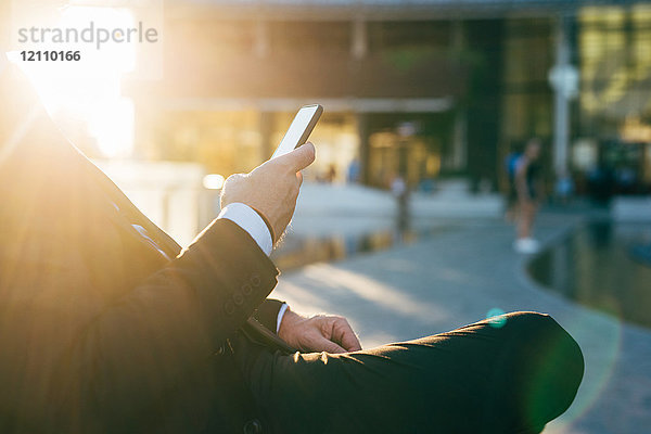 Reifer Geschäftsmann im Freien sitzend  Smartphone benutzend  Mittelteil