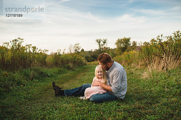 Tochter sitzt auf dem Schoß des Vaters auf Gras