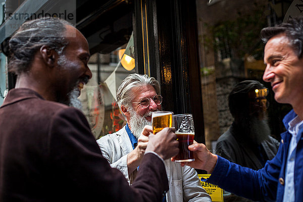 Drei reife Männer  die vor der Kneipe stehen  Biergläser halten und einen Toast ausbringen
