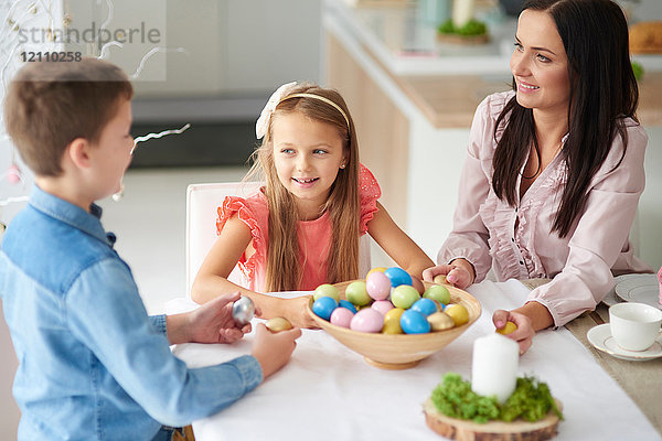 Mädchen mit Bruder und Mutter bereitet bunte Ostereier am Esstisch zu