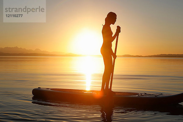 Junge Mädchen paddeln auf dem Wasser  bei Sonnenuntergang