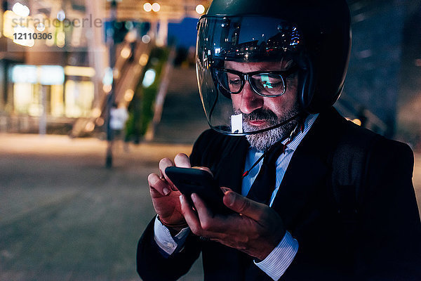 Reifer Geschäftsmann nachts im Freien  mit Motorradhelm  mit Smartphone