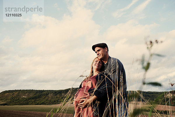 Porträt eines glücklichen schwangeren  mittleren Erwachsenenpaares auf Feldern