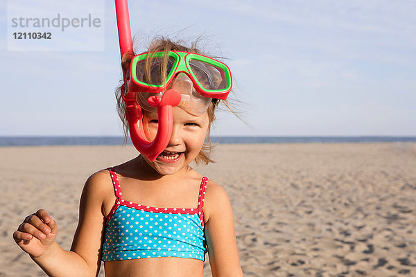 Mädchen am Strand mit Schnorchel  das lächelnd in die Kamera schaut