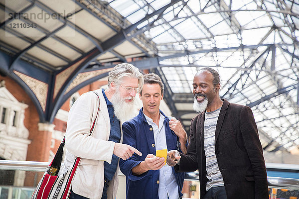 Drei reife Männer am Bahnhof mit Blick auf das Smartphone