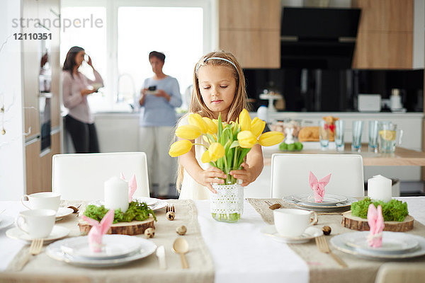 Mädchen arrangiert gelbe Tulpen am Ostertisch