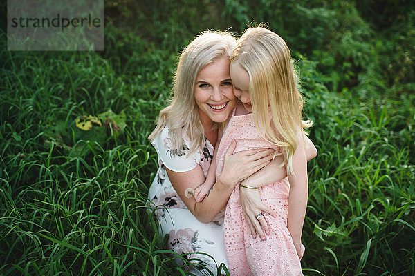 Mutter und Tochter im hohen Gras schauen lächelnd in die Kamera