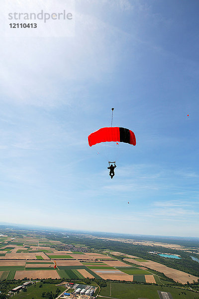 Fallschirmspringer fliegt mit Fallschirm gegen den Himmel über ländlichen Feldern